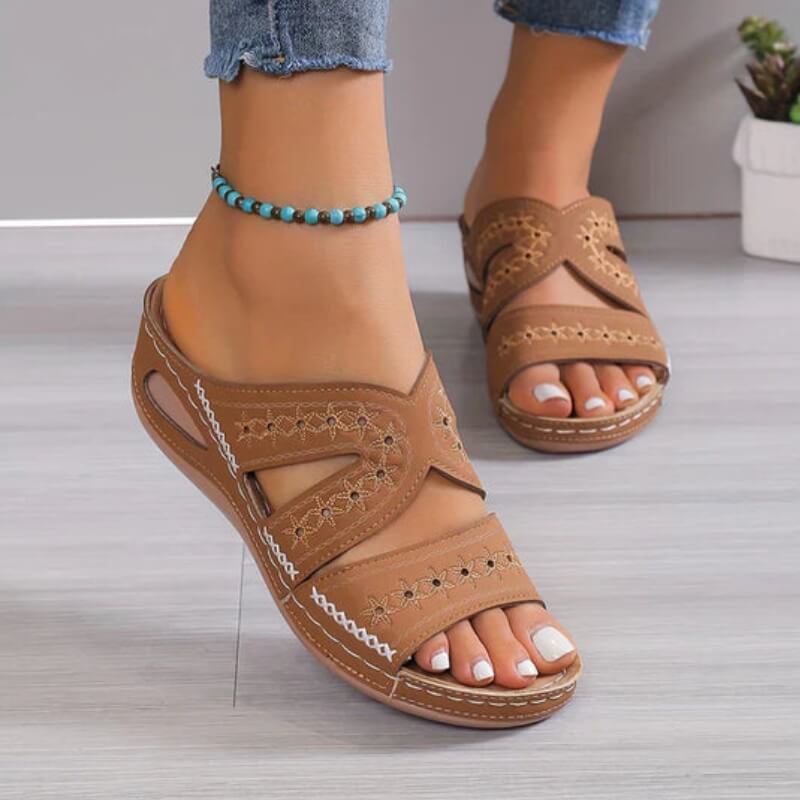Sandales marron pour femme avec détails ajourés et couture blanche, portées en intérieur sur sol clair.