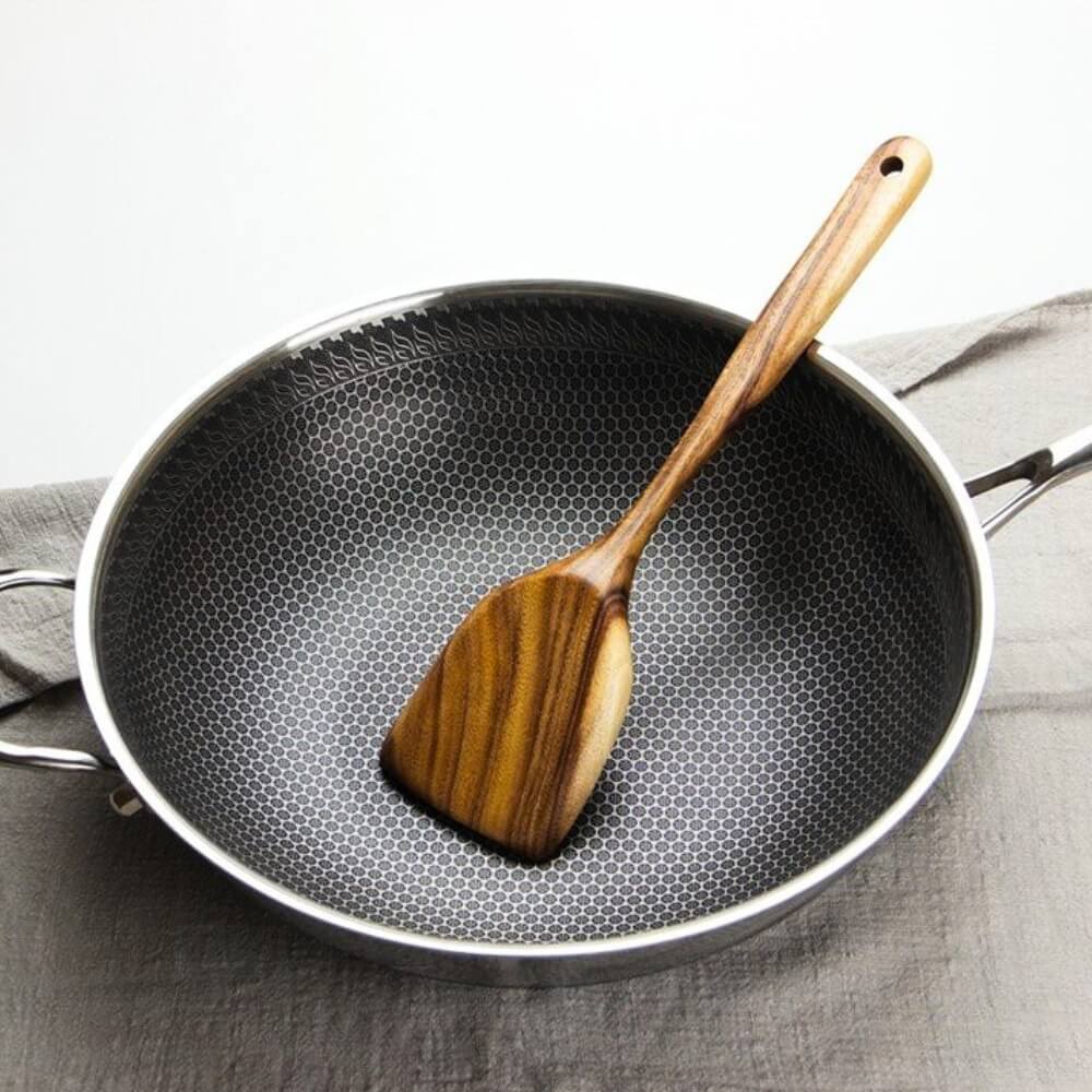 Spatule en bois lisse posée dans une poêle en inox à fond alvéolé.