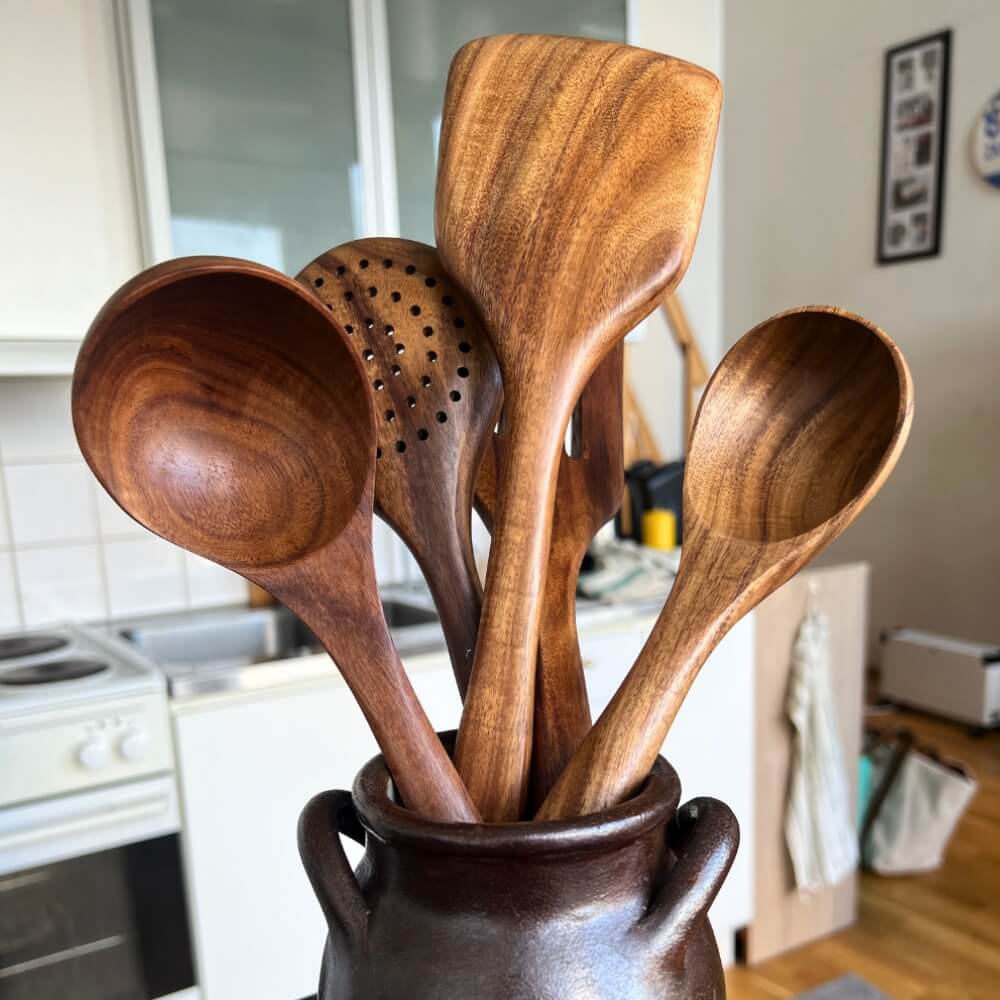 Ustensiles en bois naturel disposés dans un pot rustique en céramique dans une cuisine lumineuse.