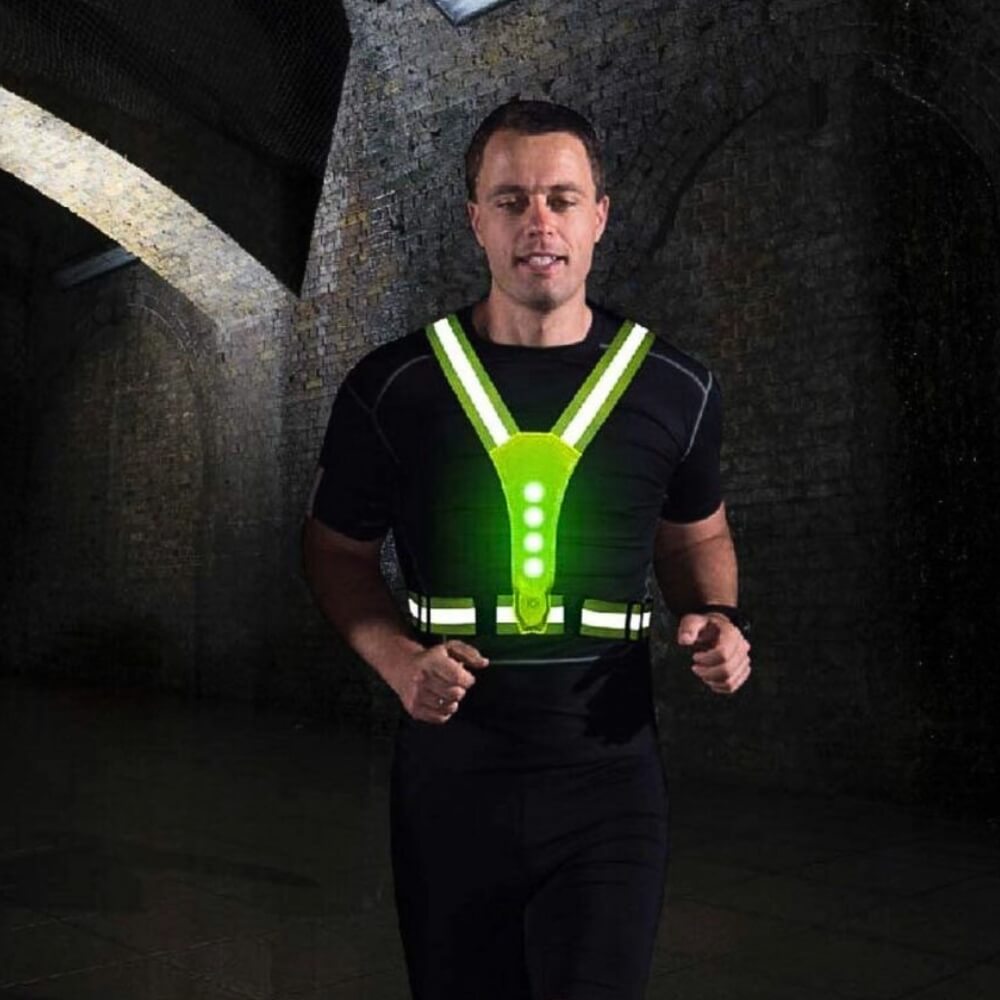 Joggeur portant un gilet réfléchissant LED vert pour une course nocturne dans un tunnel.