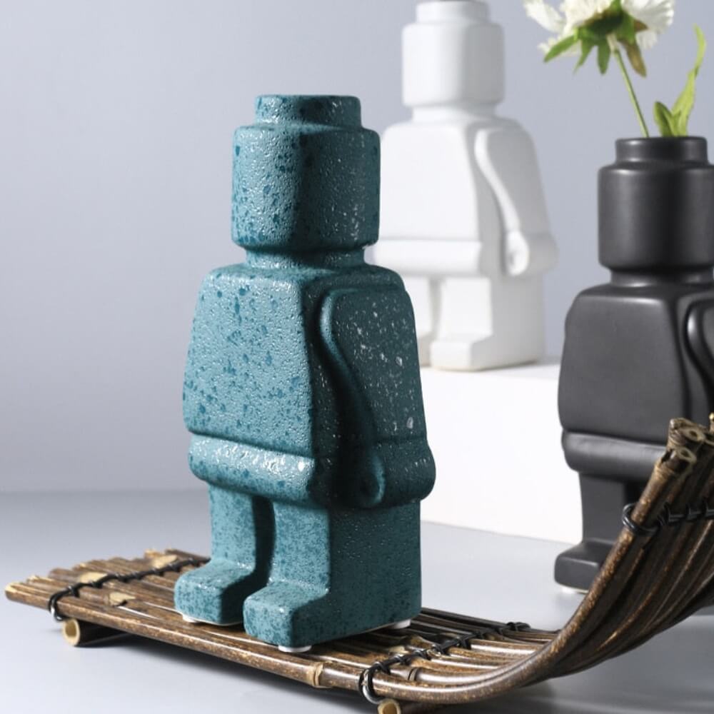 Vase design en forme de personnage LEGO vert avec finition texturée, devant d'autres vases décoratifs